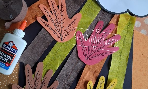 Fall craft supplies, including paper leaves, a cloud with a face, streamers, glue, and colored paper, arranged on a table. @GLUEDTOMYCRAFTS watermark is visible in the image.