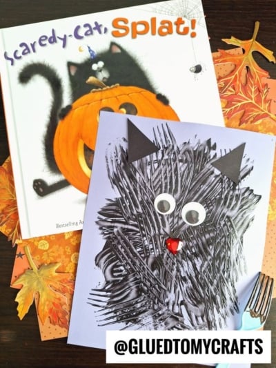 Childrens book Scaredy-Cat, Splat! with a black cat on a pumpkin, next to a handmade fork painted cat craft on purple paper, surrounded by autumn leaves and a @GLUEDTOMYCRAFTS label.
