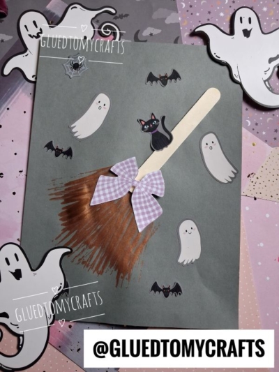 A Halloween craft featuring a fork painted witch broom with a cat, purple bow, and ghost and bat cutouts on a dark background, with @GLUEDTOMYCRAFTS watermarks.