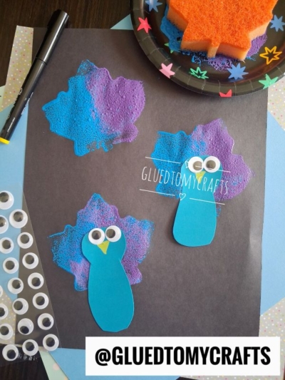 Craft a charming scene with blue and purple sponge-painted shapes, two blue paper penguins with googly eyes on black paper, and fun extras like a sticker sheet, marker, and paint-covered sponge. This creative project makes a perfect addition to your collection of FALL CRAFTS FOR KIDS. @GLUEDTOMYCRAFTS text at the bottom.