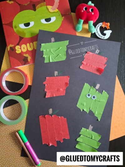 Apple-themed kids craft with red and green paper strip apples on black paper, markers, washi tapes, painter’s tape craft ideas, a Sour Apple book, a plush apple, and craft supplies, all arranged on an orange polka dot background.