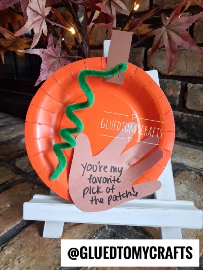 An orange paper plate pumpkin craft with a green pipe cleaner stem and a brown paper hand cutout labeled You’re my favorite pick of the patch! displayed on a small easel—this is one of the cutest FALL CRAFTS FOR KIDS to brighten up your autumn décor.