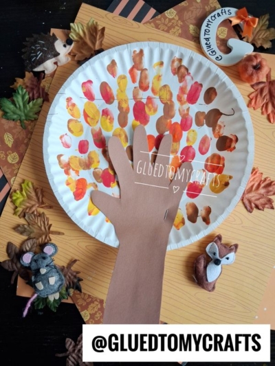 Paper plate autumn tree craft with a handprint trunk, painted leaves in fall colors, and surrounded by felt animal figures (mouse, hedgehog, fox) and artificial leaves—this is one of the perfect FALL CRAFTS FOR KIDS. @GLUETOMYCRAFTS label at the bottom.