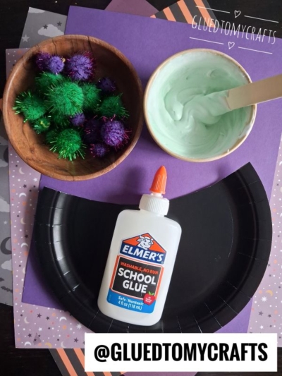 Black paper plate, Elmers glue, a bowl of green slime with a wooden stick, and a bowl of sparkly pom-poms on purple paper with stars. @GLUEDTOMYCRAFTS written at the bottom.