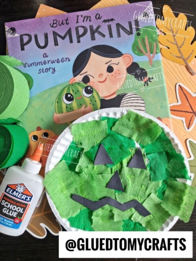 A childrens pumpkin-themed book, green and orange craft supplies, Elmers glue, and a paper plate decorated as a green jack-o-lantern are arranged together—perfect inspiration for your summer craft ideas. @GLUEDTOMYCRAFTS appears at the bottom.