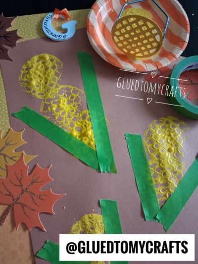Brown paper with yellow paint shapes made using a potato masher, green tape as stems, paper leaves, paint, and a roll of green tape. @GLUEDTOMYCRAFTS label appears at the bottom.
