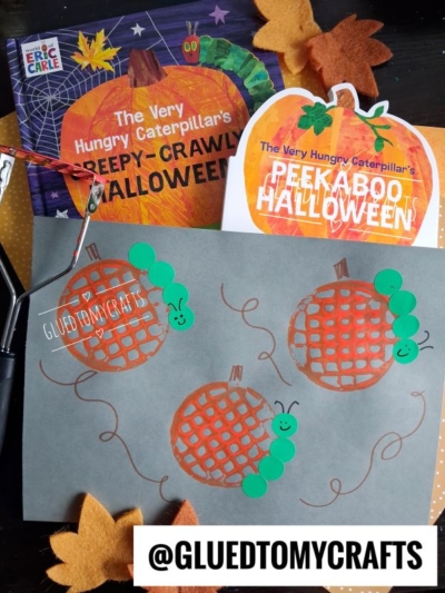 Craft project with paper caterpillars and pumpkins, felt leaves, and two The Very Hungry Caterpillar Halloween books—perfect for FALL CRAFTS FOR KIDS. @GLUEDTOMYCRAFTS text at the bottom. Smiling green caterpillar faces drawn on the paper.