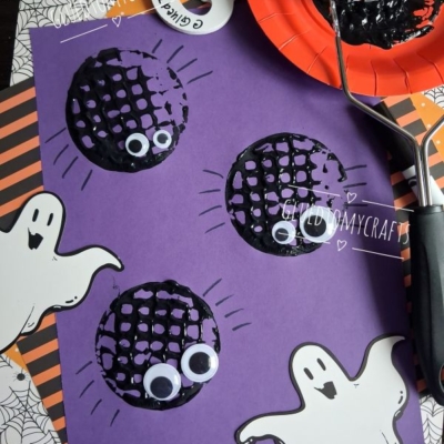 Purple paper with black painted circles, googly eyes, and ghost cutouts, showing a Halloween craft project. A potato masher with black paint is nearby. @GLUEDTOMYCRAFTS text is at the bottom.