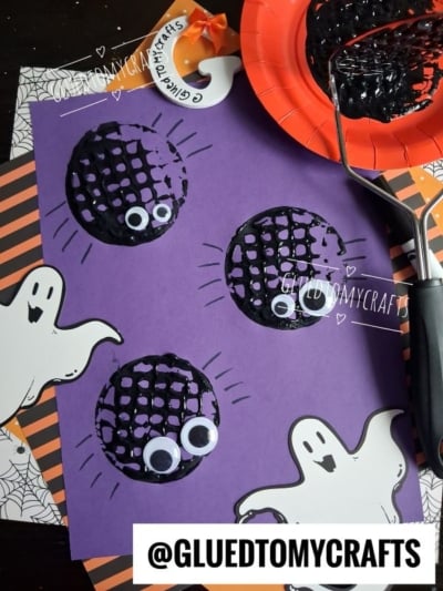 Purple paper with black painted circles, googly eyes, and ghost cutouts, showing a Halloween craft project. A potato masher with black paint is nearby. @GLUEDTOMYCRAFTS text is at the bottom.