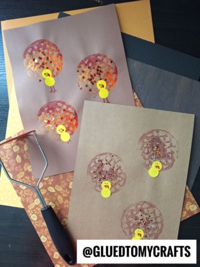 Two pieces of brown paper show turkey crafts made from painted potato masher prints for feathers and yellow paper for bodies, with craft supplies visible nearby. @GLUEDTOMYCRAFTS is written at the bottom.