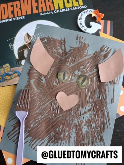 A brown paper craft owl with textured paint made using a fork, inspired by a fork painted werewolf technique, surrounded by books and labeled with the handle @GLUEDTOMYCRAFTS.
