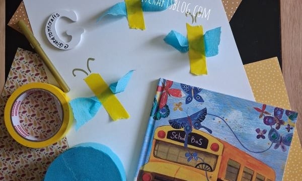 A butterfly craft project with blue and yellow paper butterflies, crafting materials, and the book Butterflies on the First Day of School displayed on patterned paper.