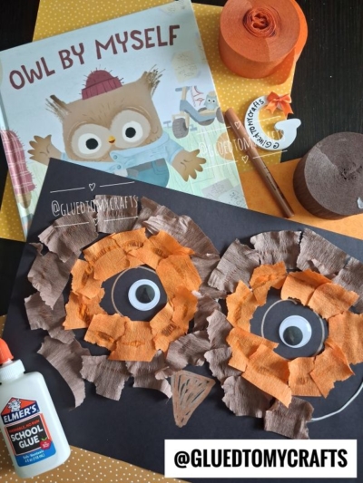 A children’s Owl By Myself book, glue, and orange and brown paper strips surround a charming mosaic owl craft on black paper. Craft materials and the @GLUEDTOMYCRAFTS label are also visible.