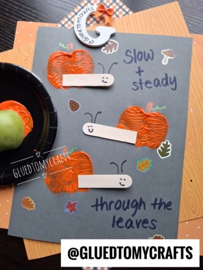 A fall-themed craft features orange-painted pumpkins, craft stick snails, leaf stickers, and the text slow + steady through the leaves on dark paper. A green apple and paint plate are nearby. @GLUEDTOMYCRAFTS is labeled.