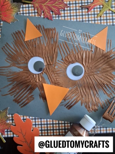 A brown fork-painted owl face on blue paper with googly eyes and an orange paper beak and ears, surrounded by fall leaves and a plaid tablecloth—perfect for FALL CRAFTS FOR KIDS. Text reads @GLUETOMYCRAFTS.