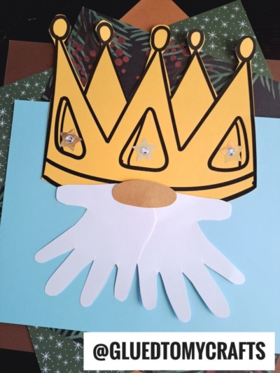 A handprint king gnome paper craft features a king’s face with a yellow crown and white beard, both made from cut-out hand shapes, displayed on colorful paper backgrounds.