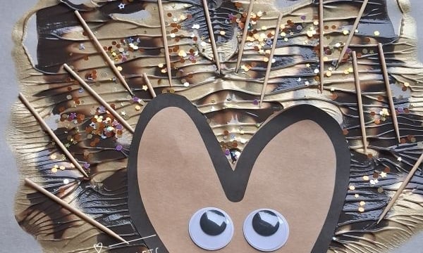 A handmade hedgehog craft using googly eyes, paper, toothpicks, paint, and glitter is shown on a gray background with autumn leaf cutouts. @GLUEDTOMYCRAFTS is labeled at the bottom.