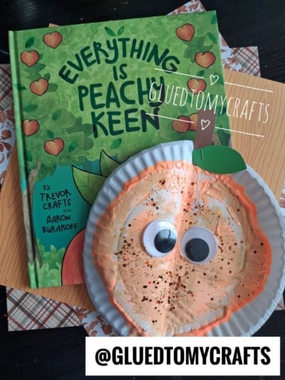 A childrens book titled Everything is Peachy Keen is next to a paper plate peach craft with big googly eyes. The craft is painted peach and sprinkled with glitter. Text reads @GLUEDTOMYCRAFTS..