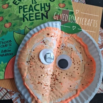 A peach-themed kids craft made from a paper plate with googly eyes and glitter sits on a table, next to the book Everything Is Peachy Keen. Instagram handle @GLUEDTOMYCRAFTS is shown.