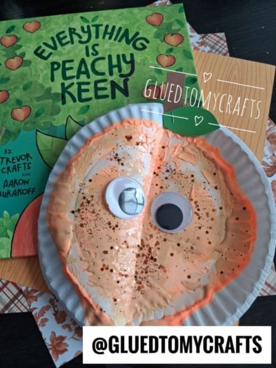 A peach-themed kids craft made from a paper plate with googly eyes and glitter sits on a table, next to the book Everything Is Peachy Keen. Instagram handle @GLUEDTOMYCRAFTS is shown.