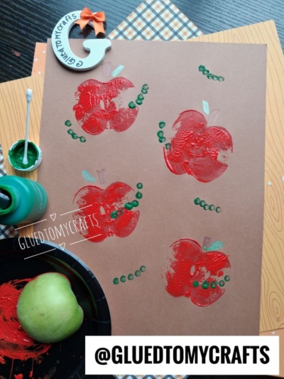 A brown paper shows an APPLE STAMPED CRAFT, featuring apple prints made with red paint and a green apple, accented with green paint dots. Paint and a painted apple are nearby. @GLUEDTOMYCRAFTS is at the bottom.