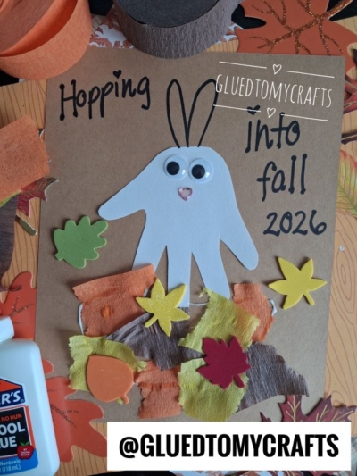 A fall-themed craft perfect for FALL CRAFTS FOR KIDS features a handprint bunny, felt leaves, googly eyes, and “Hopping into fall 2026” on brown paper, surrounded by autumn decorations and a glue bottle.