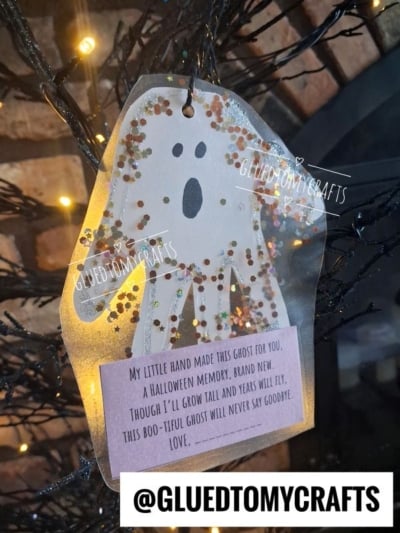 A glittery ghost ornament shaped from a handprint hangs on a black tree. A purple note beneath reads, My little hand made this ghost for you... This boo-tiful ghost will never say goodbye. Love..