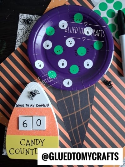 A purple paper plate with ghost and green dot stickers, a DIY candy corn countdown showing 60, and Halloween-themed paper, marker, and plastic spider—perfect inspiration for Halloween Crafts for Kids. Text: @GLUEDTOMYCRAFTS.