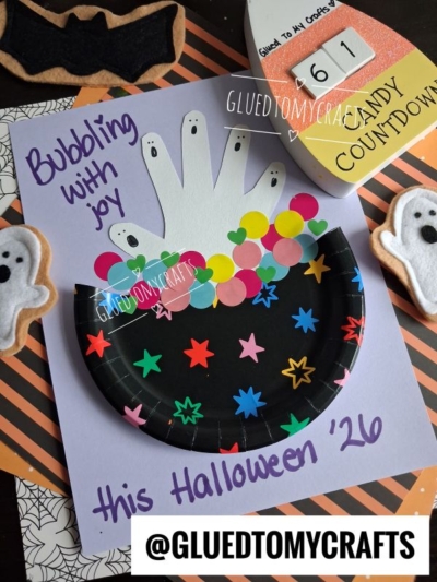 A Halloween craft with a black, starry paper plate and handprint ghosts, colorful dots as bubbles, and “Bubbling with joy this Halloween 26” written on purple paper. Perfect for Halloween Crafts for Kids, ghost felt figures and a countdown block are nearby.