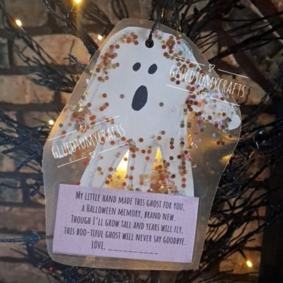 A paper ghost craft with glitter and a poem hangs on a black tree. The poem is about a handprint ghost that will never say goodbye. The Instagram handle @GLUEDTOMYCRAFTS is at the bottom.