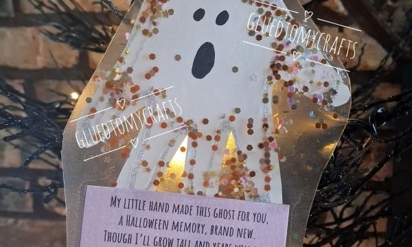 A paper ghost craft with glitter and a poem hangs on a black tree. The poem is about a handprint ghost that will never say goodbye. The Instagram handle @GLUEDTOMYCRAFTS is at the bottom.