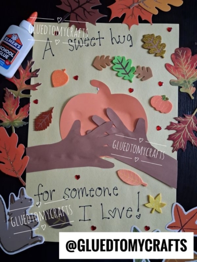 A fall-themed craft with paper hands hugging an orange pumpkin, surrounded by cut-out leaves, acorns, and a squirrel on yellow paper. Text reads: A sweet hug for someone I love! This adorable project is one of the best FALL CRAFTS FOR KIDS, with a glue bottle and hearts visible.