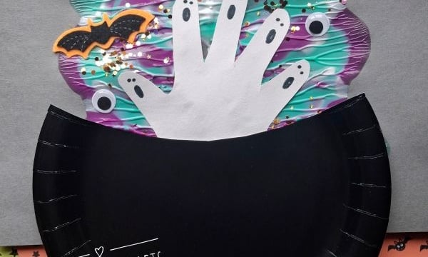 A paper craft shows a black cauldron with handprint ghosts, bats, and colorful swirls rising from it, on a gray background. The handle @GLUEDTOMYCRAFTS is written at the bottom.