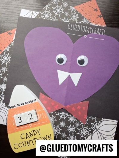 A purple paper vampire face with googly eyes and paper fangs is displayed on Halloween-themed paper, next to a candy corn-shaped Candy Countdown craft—perfect Halloween Crafts for Kids! @GLUEDTOMYCRAFTS is shown at the bottom.