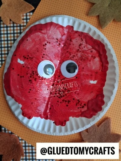 A bright red, cranberry paint splat on a white paper plate with two large googly eyes attached in the center.