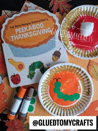 Childrens craft scene with a Peekaboo Thanksgiving book, paper plate crafts resembling a caterpillar and pie, glue sticks, and colorful paper leaves. Perfect for FALL CRAFTS FOR KIDS, the caterpillar is made from green paper circles glued on a plate.