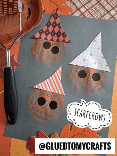 Three waffle-printed scarecrow faces with paper hats on blue paper, surrounded by autumn-themed decorations and a potato masher. Text reads SCARECROWS and @GLUEDTOMYCRAFTS.