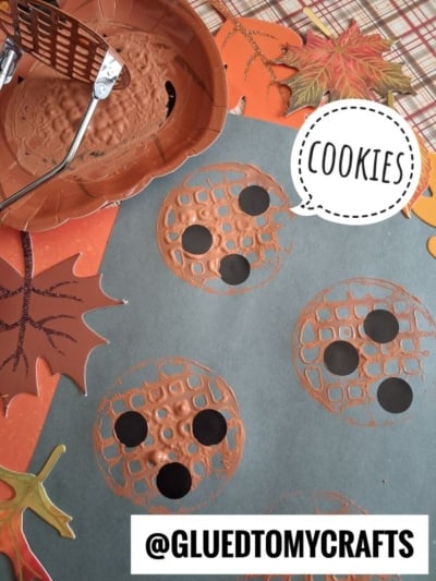 A craft project shows painted cookies made by stamping brown paint with a potato masher on blue paper, topped with black circles for chips. Fall leaves and a sign saying Cookies decorate the scene.