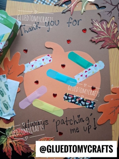 A paper pumpkin decorated with colorful bandages and red heart gems, surrounded by autumn leaves and bandage wrappers. This fun project is perfect for FALL CRAFTS FOR KIDS. The message reads, Thank you for patching me up!.