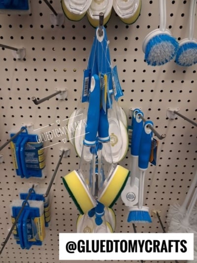 Various cleaning brushes and sponges with blue handles hang on a white pegboard display. The text @GLUEDTOMYCRAFTS appears at the bottom.