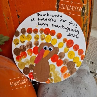A round canvas shows a thumbprint turkey craft with googly eyes, surrounded by colorful dots. Text reads, Thumb-body is thankful for you! Happy Thanksgiving 2026. Pumpkins sit nearby. @GLUEDTOMYCRAFTS is also shown.