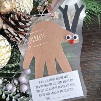 A handmade reindeer ornament made from a paper handprint, featuring googly eyes and a red nose, with a printed poem attached at the bottom.