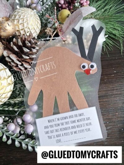 A handmade reindeer ornament made from a paper handprint, featuring googly eyes and a red nose, with a printed poem attached at the bottom.