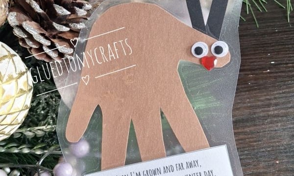 A handmade reindeer ornament made from a paper handprint, featuring googly eyes and a red nose, with a printed poem attached at the bottom.