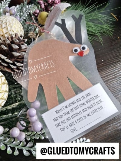 A DIY reindeer ornament made from a childs handprint cutout with googly eyes, a red nose, and a tag featuring a poem about keeping a piece of them for the holidays.