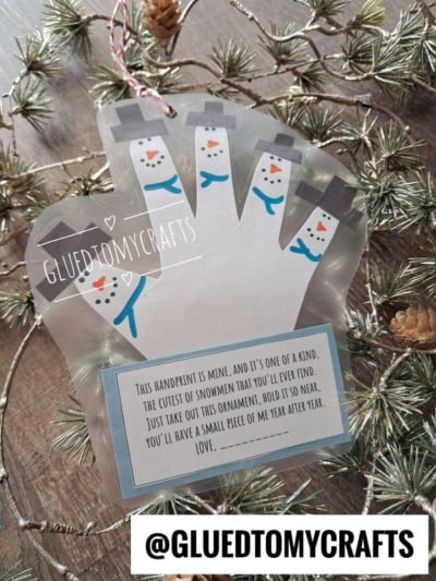 Handprint snowman ornament with a poem about a keepsake, resting on a pine branch.