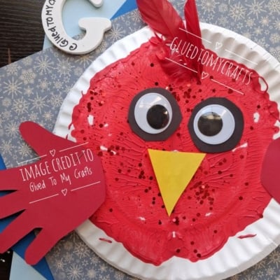 A paper plate craft of a red bird with googly eyes, a yellow beak, and a red paper handprint wing.