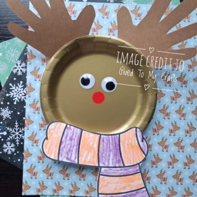 A gold paper plate reindeer craft with handprint antlers and a hand-drawn striped scarf.