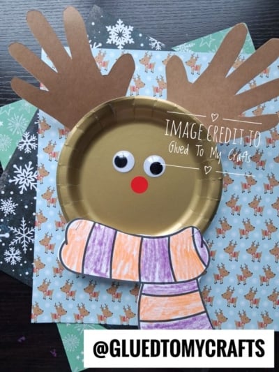 A gold paper plate reindeer craft with handprint antlers and a hand-drawn striped scarf.