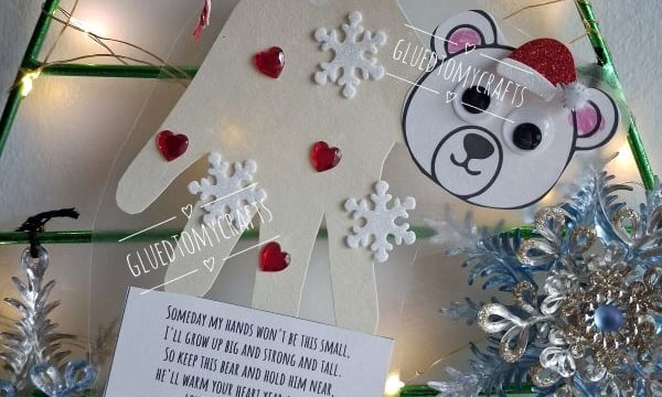 A handmade ornament featuring a paper handprint, a polar bear face, and a poem about growing up, decorated with red hearts and white snowflakes.